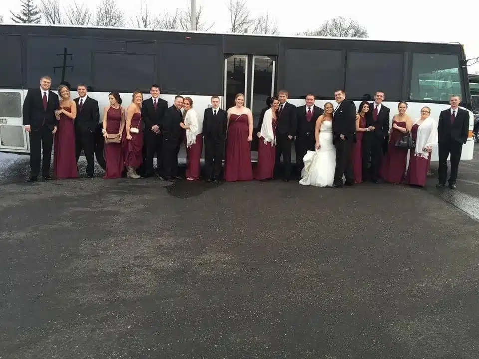 Wedding party in formal attire in front of a party bus.